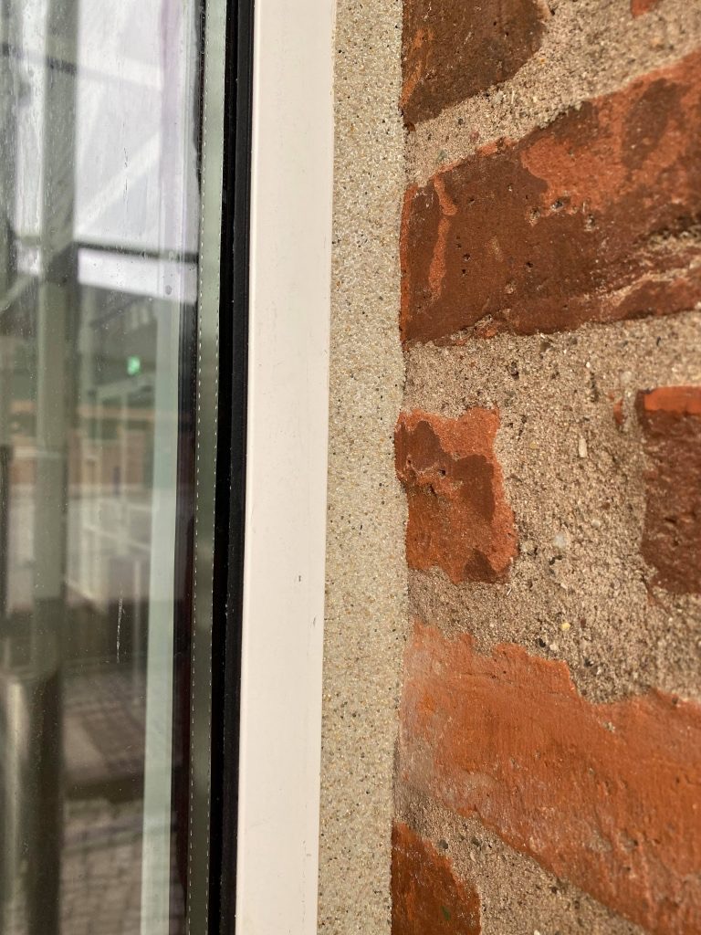 Nærbillede af en besandet fuge mellem vinduesramme og murværk